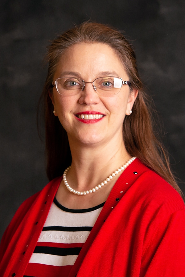 Picture of Sandra Hiebert, white woman, with long brown hair and glasses wearing a professional read sweater.